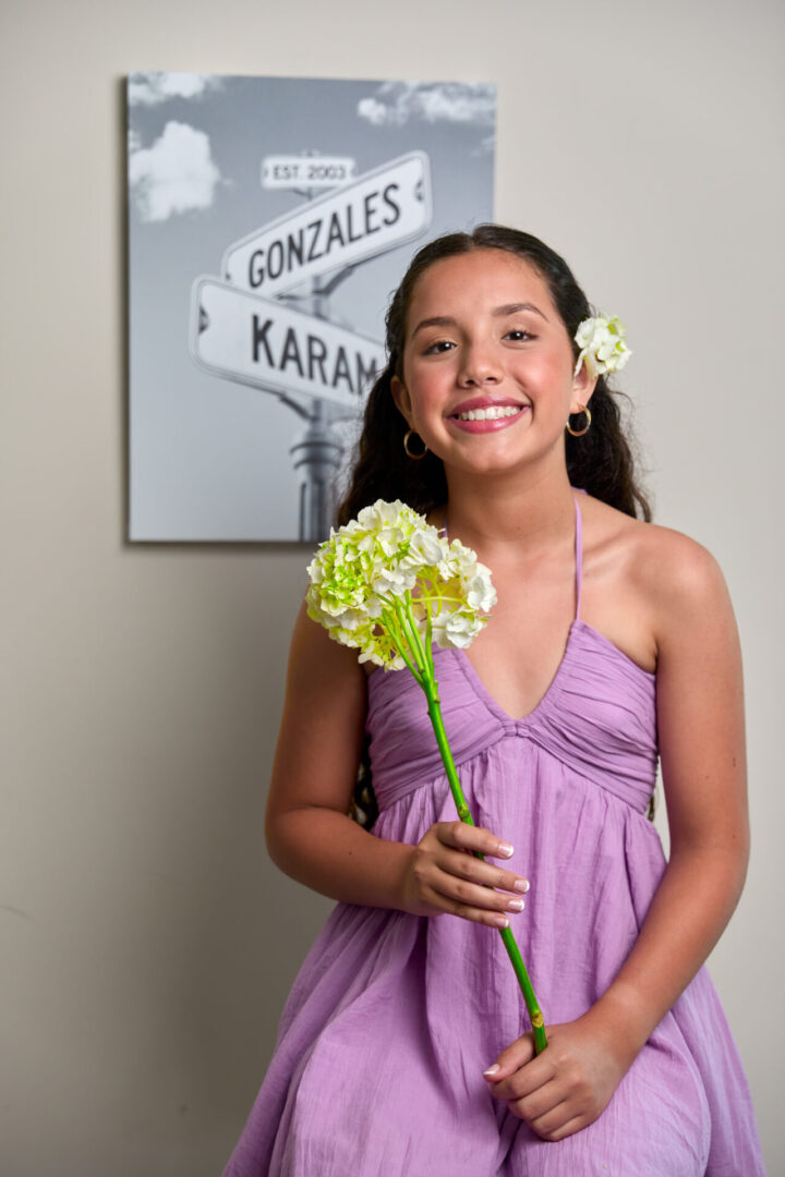 A girl in purple dress holding flowers and smiling.