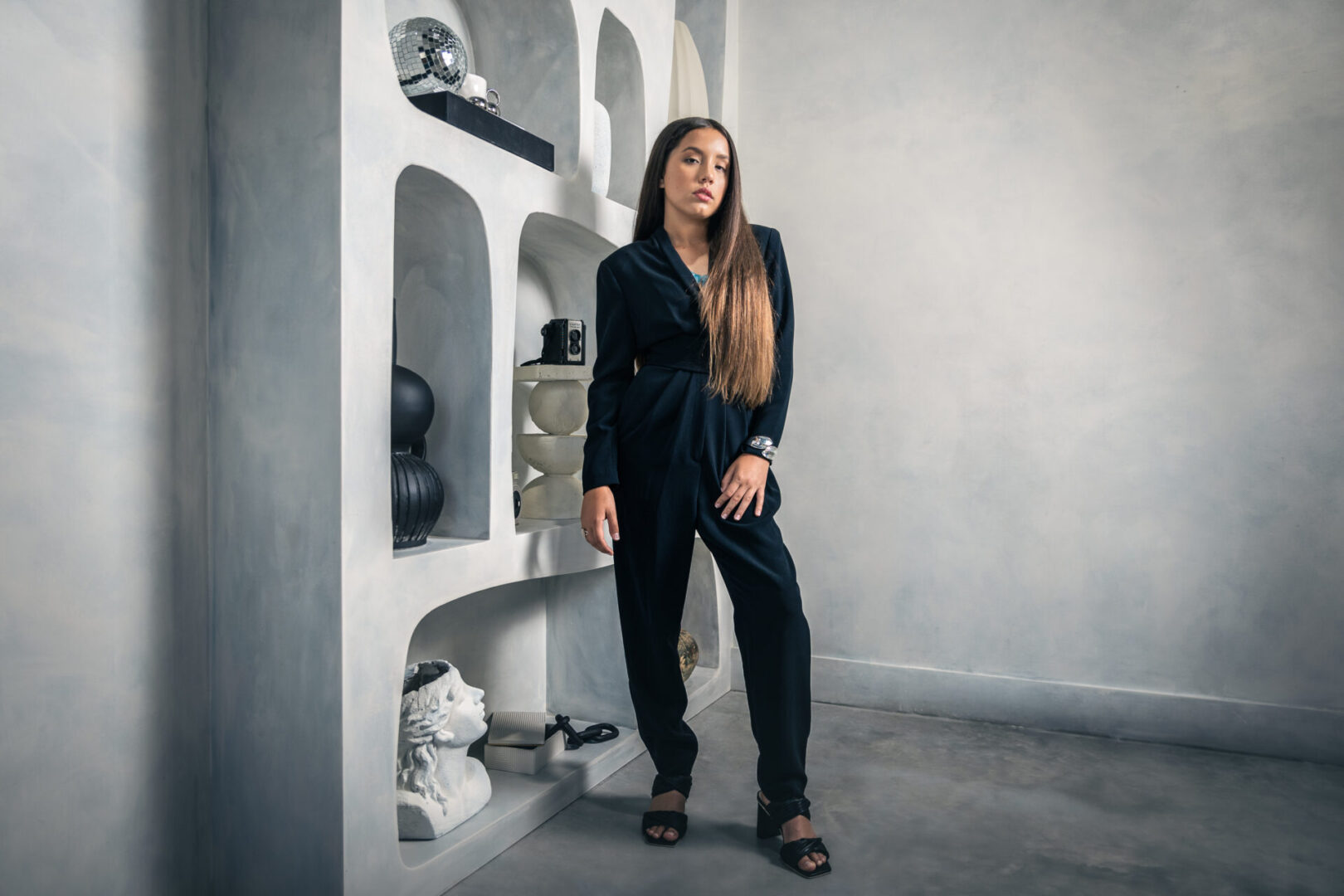 A woman in black outfit standing next to a wall.